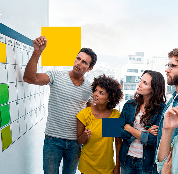 Work team conducting a strategic planning session in front of a wall schedule in a bright office setting.